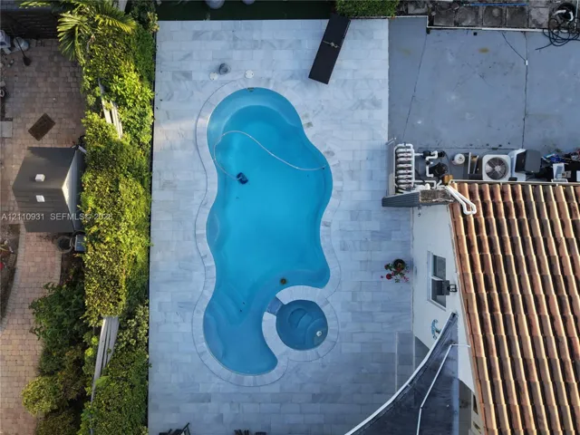 Freeform swimming pool featuring an integrated spa, surrounded by stone-tile decking