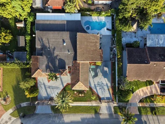 Aerial perspective of a multi-section roofline, expansive concrete driveway, and backyard pool area with integrated hardscaping