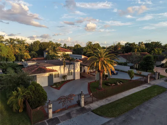 Single-story residence featuring a tile roof, gated concrete driveway, metal perimeter fencing, and mature palm landscaping