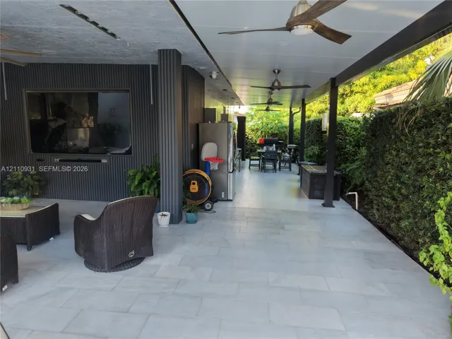 Covered patio featuring large-format stone-style tile flooring, recessed ceiling lighting, multiple overhead fans, and vertical-slat wall accents