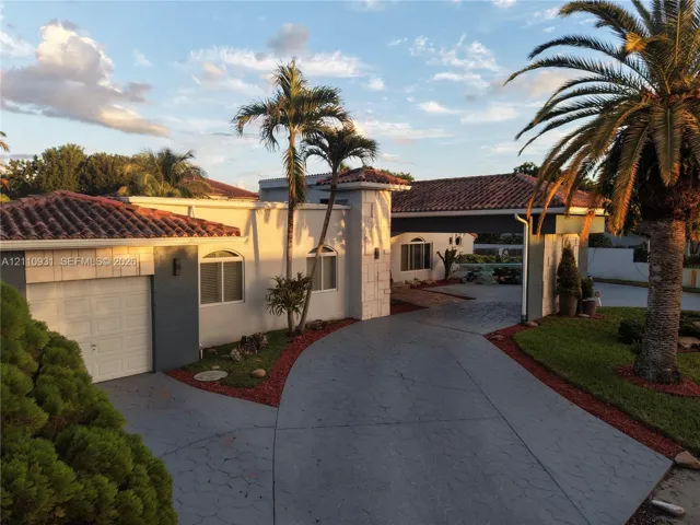 Stucco exterior featuring arched windows, a multi-car covered porte-cochère, decorative stone accents, and a tile roof
