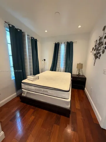 Room featuring wood-finish flooring, recessed lighting, and multiple windows with dual-layer rod-mounted window treatments