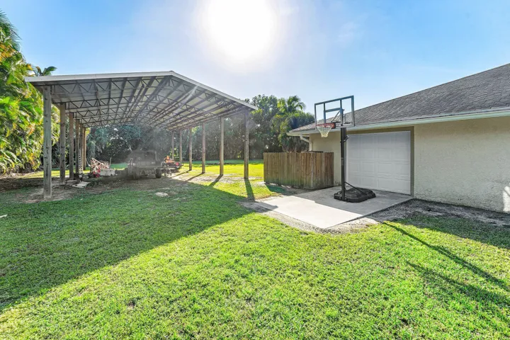Exterior space featuring an expansive covered carport, a concrete pad, a garage, and a grass lawn