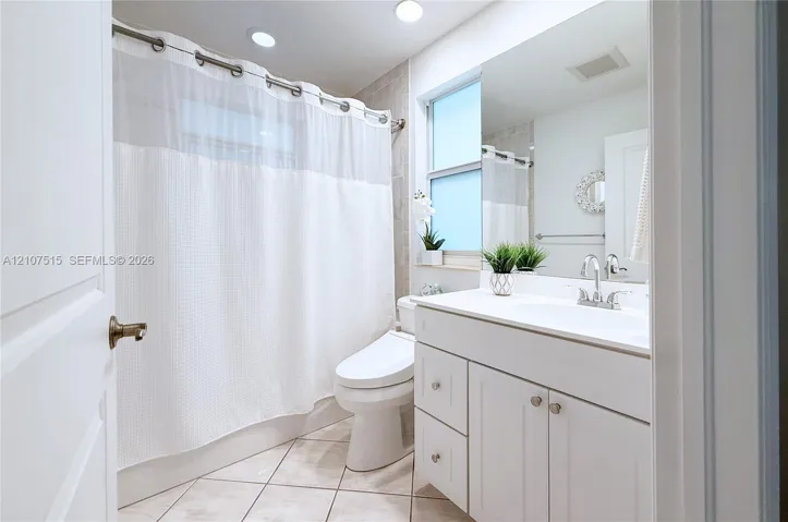 Bathroom featuring a white vanity cabinet with an integrated sink, large wall-mounted mirror, neutral tile flooring, and a shower-tub combination with tile surround