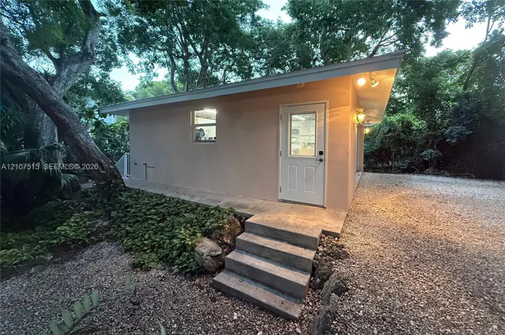 Detached structure with stucco exterior, single-slope roofline, concrete entry steps, and gravel ground cover