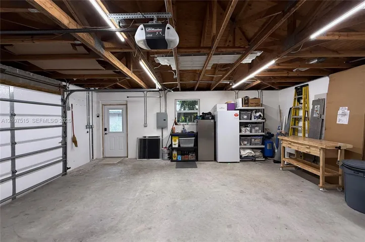 Garage featuring exposed wood beam ceiling, linear LED lighting, concrete flooring, and a dedicated entry door