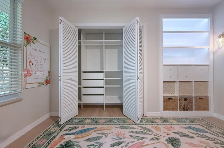 Second bedroom. Custom closet featuring white louvered doors, integrated shelving, and a built-in drawer system