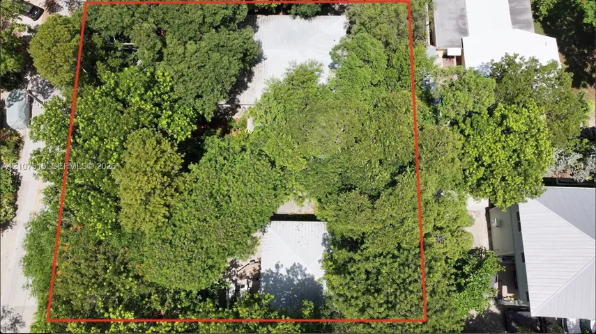 Aerial view of a lot featuring mature tree canopy, cleared pathways, and metal roof structures