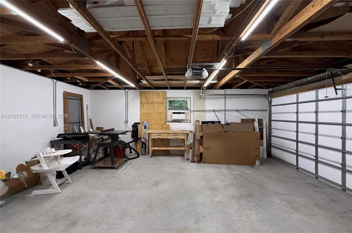 Attached garage featuring concrete flooring, exposed wood truss ceiling, LED linear lighting, and a window-mounted climate control unit