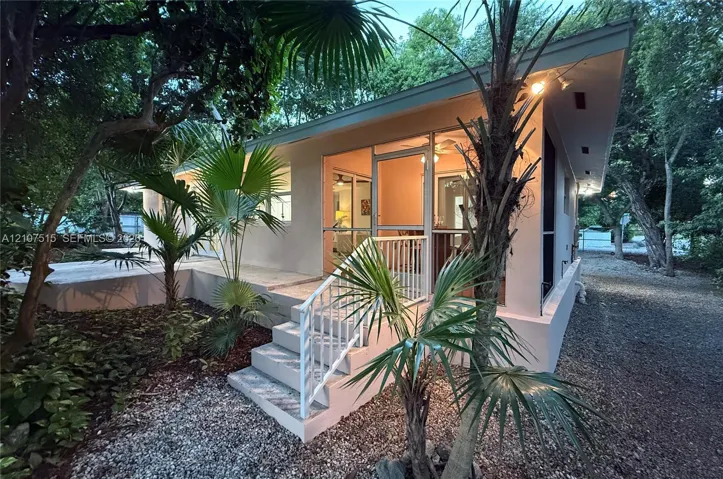 Single-story exterior featuring a screened-in porch, concrete stairs with metal railings, a concrete patio, and mature palm landscaping