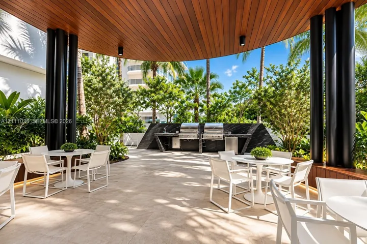 Covered outdoor kitchen featuring dual stainless steel grills, stone-finish countertops, wood-paneled ceiling, and large-format tile flooring