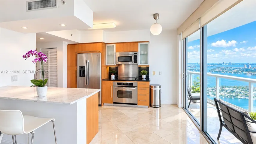 Kitchen featuring wood-finish cabinetry, stainless steel appliances, stone-topped island, polished tile flooring, and floor-to-ceiling glass sliding doors