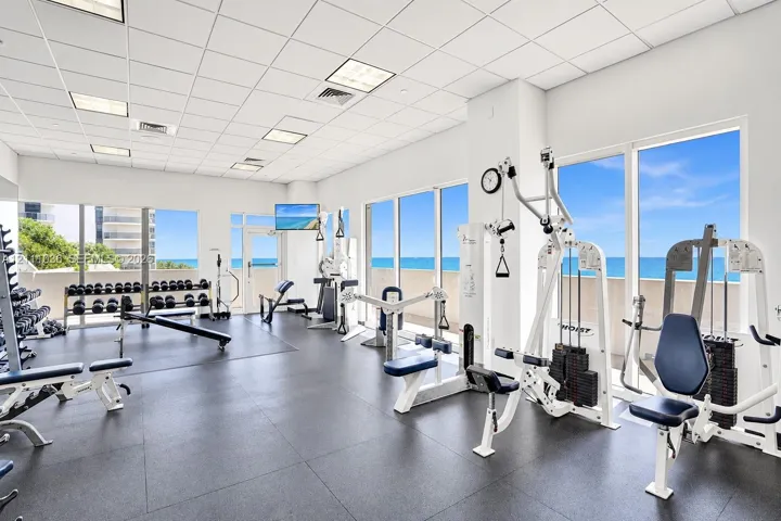 Fitness center featuring floor-to-ceiling windows, ocean horizon backdrop, drop-ceiling grid, and durable rubberized flooring