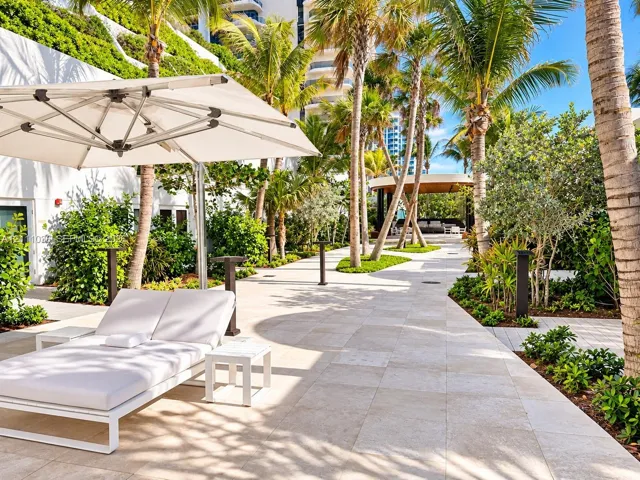 Outdoor patio featuring natural stone paving, mature palm trees, tiered tropical landscaping, and a covered pavilion