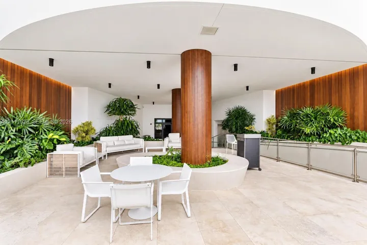 Covered outdoor terrace featuring large-format stone tile flooring, warm wood-paneled walls, integrated recessed lighting, and a central structural column with a circular built-in planter
