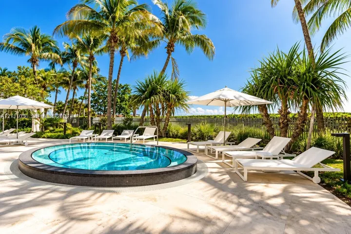 Circular swimming pool with dark tile surround, light-toned stone decking, and mature palm landscaping