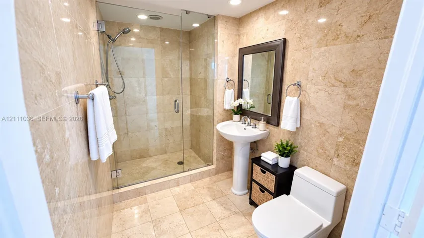 Full-height natural stone wall tiling, walk-in glass-enclosed shower, pedestal sink, and polished chrome fixtures
