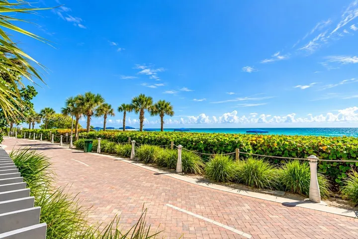 Brick-paver pathway featuring rope fencing, ornamental grasses, and mature palm trees
