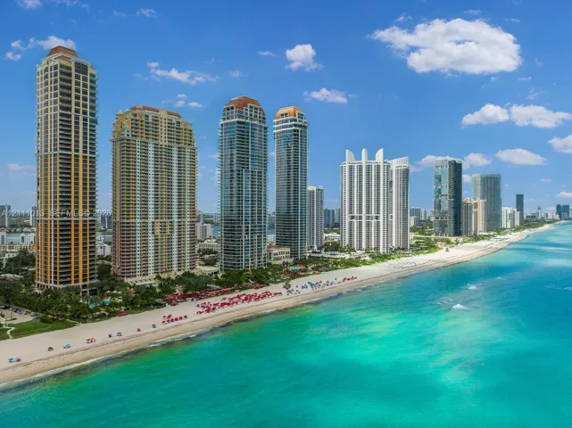 High-rise residential towers positioned along a sandy coastline featuring direct ocean access and expansive waterfront frontage