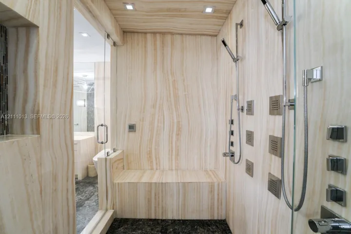 Walk-in shower featuring floor-to-ceiling stone wall cladding, built-in stone bench, multi-head chrome shower system, and frameless glass enclosure