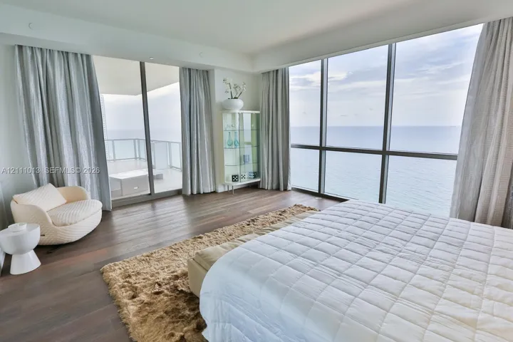 Floor-to-ceiling glass walls, wood-finish flooring, and a private balcony featuring a glass railing