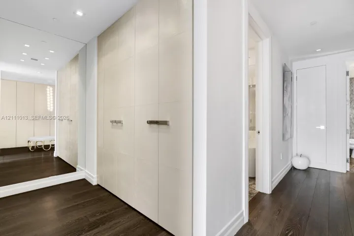 Full-height cabinetry with smooth, panel-style doors, polished hardware, integrated floor-to-ceiling mirrored wall, recessed ceiling lighting, and dark wood-finish flooring