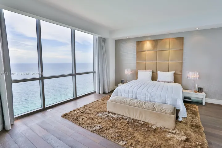 Floor-to-ceiling windows featuring ocean scenery, wood-finish flooring, and a floor-to-ceiling upholstered grid headboard