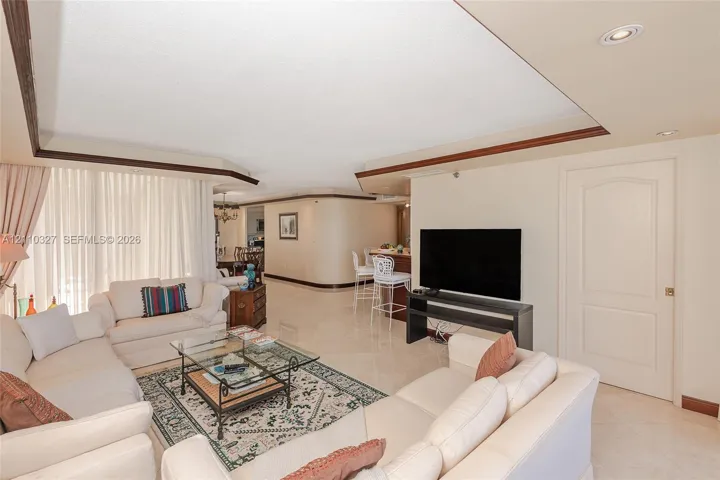 Open-concept interior featuring tray ceilings, neutral tile flooring, built-in breakfast bar, and recessed lighting