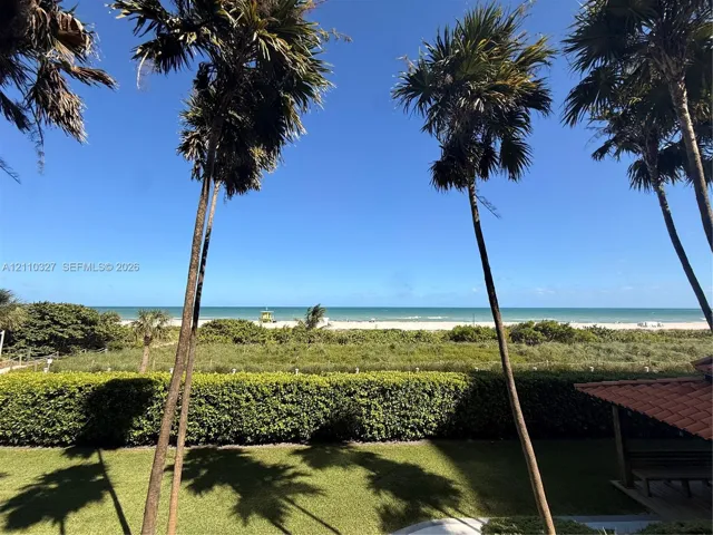 Expansive outdoor space featuring manicured lawn, mature palm trees, sculpted privacy hedging, and unobstructed ocean frontage