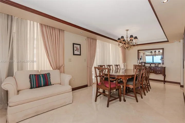 Dining area featuring recessed ceiling detail, crown molding, stone-finish flooring, and a multi-arm chandelier
