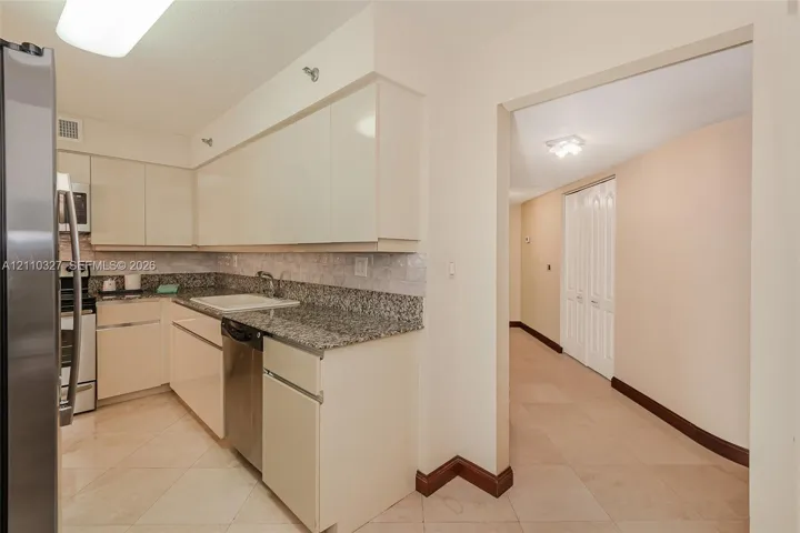 Kitchen featuring light-toned cabinetry, stone-finish countertops, stainless steel appliances, tile backsplash, and tile flooring