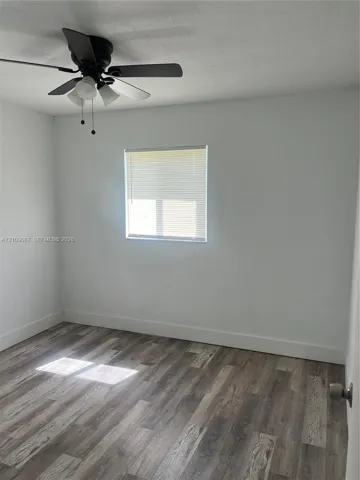 Interior room featuring wood-finish flooring, a matte black ceiling fan with integrated lighting, and a window with horizontal blinds