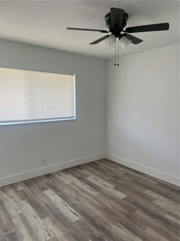 Room interior featuring wood-finish flooring, white walls, and a ceiling-mounted fan with integrated lighting
