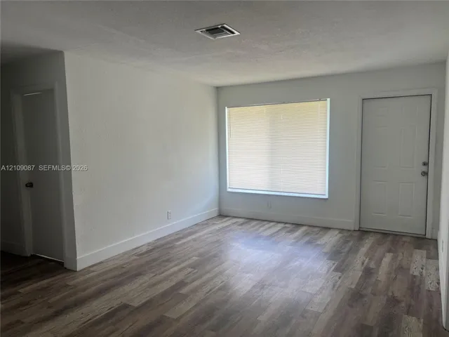 Neutral interior space featuring wood-finish flooring, a large window with pleated blinds, and a six-panel door