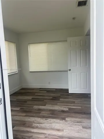 Room interior featuring wood-finish flooring, white walls, and a six-panel door
