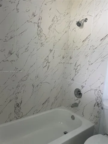 Bathtub surround featuring large-format veined tile, chrome shower head, matching chrome tub filler, and integrated pressure-balancing valve