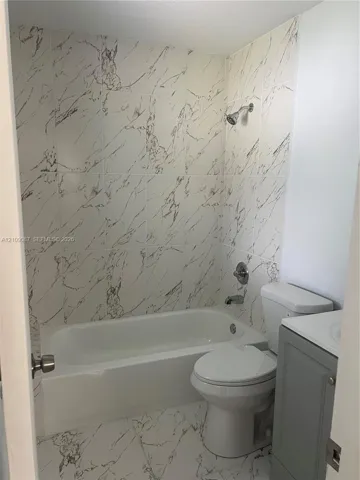Bathroom featuring large-format tile flooring and wall surrounds with a veined pattern, built-in soaking tub, chrome fixtures, and a gray vanity cabinet