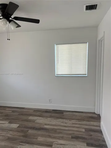 Wood-finish flooring, neutral wall tones, multi-blade ceiling fan with integrated lighting, and horizontal window blinds