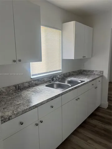 Kitchen featuring white cabinetry, stone-patterned laminate countertops, dual-basin stainless steel sink, and wood-finish flooring