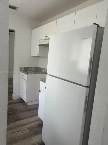Kitchen featuring white shaker-style cabinetry, high-contrast patterned countertops, a top-freezer refrigerator, and wood-finish flooring
