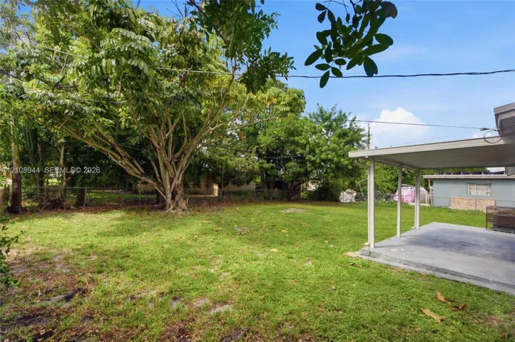 Backyard featuring a concrete patio, covered porch, mature trees, chain-link fencing, and grass lawn