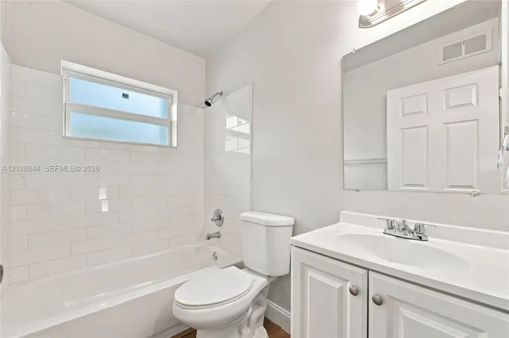 Bathroom featuring white subway tile tub surround, white vanity cabinet with an integrated sink, polished chrome plumbing fixtures, and a wall-mounted vanity mirror