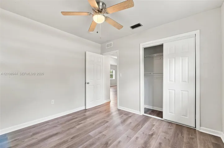 Room featuring wood-finish flooring, a ceiling fan with light fixture, and a closet with sliding paneled doors