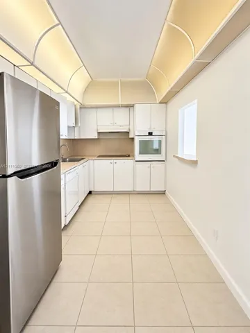 Kitchen featuring white cabinetry, stainless steel refrigerator, built-in wall oven, tile flooring, and barrel vault ceiling detail