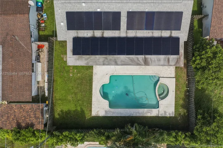 Aerial perspective featuring a shingle roof with integrated solar panels, an in-ground swimming pool with an attached spa, and a fenced yard