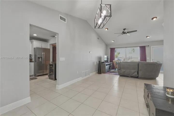 Open-concept interior featuring vaulted ceilings, oversized tile flooring, a geometric metal-frame pendant light, recessed lighting, and a ceiling fan