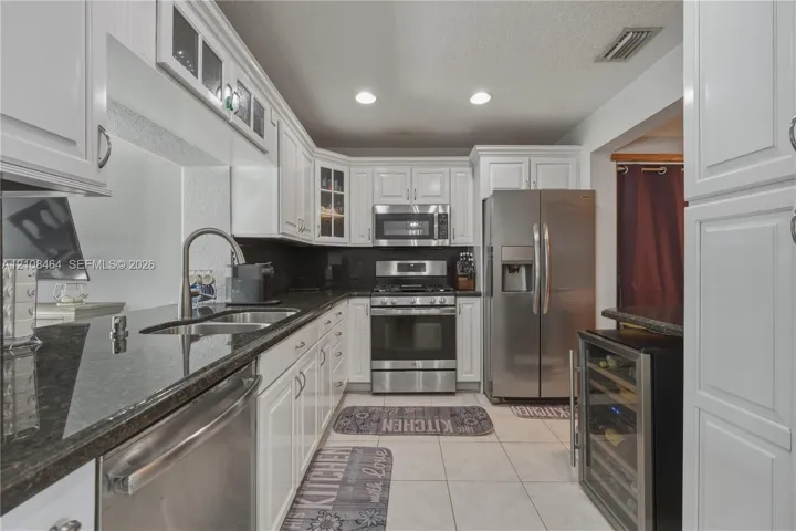 Kitchen featuring white cabinetry, stone countertops, stainless steel appliances, a built-in wine cooler, and tile flooring