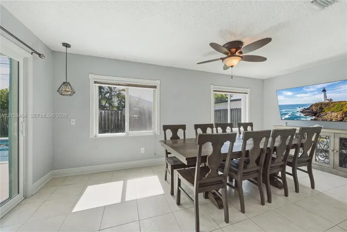 Neutral-toned room featuring ceramic tile flooring, dual-pane windows, sliding glass door, ceiling fan with light kit, and geometric pendant lighting