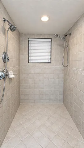 Walk-in shower featuring dual wall-mounted shower heads, ceramic tile surround with decorative inlay, recessed ceiling lighting, and window with integrated blinds