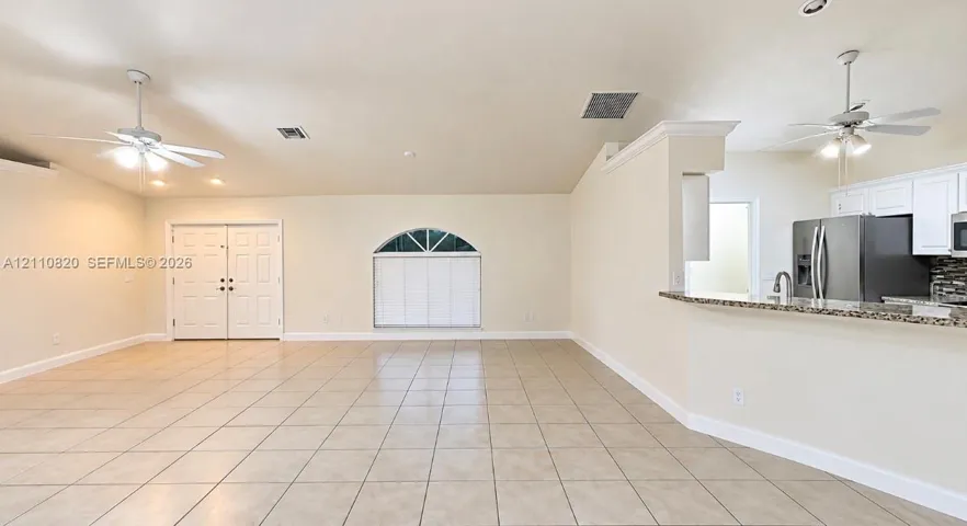 Open-concept interior featuring light-toned tile flooring, dual ceiling fans, a vaulted ceiling, arched window, and a kitchen breakfast bar with stone-finish countertops